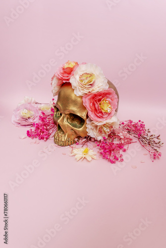 Fototapeta Naklejka Na Ścianę i Meble -  A golden skull adorned with flowers on a smooth pink surface