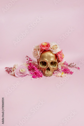 Fototapeta Naklejka Na Ścianę i Meble -  The golden skull looks pretty and flirty surrounded by dried flowers and plants with branches on a soft pink surface