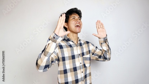 Angry young Asian man raising hands and shouting with aggressive expression