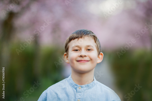 Cute smiling boy walks along the street of cherry blossoms. Happy children. Warm bright spring.