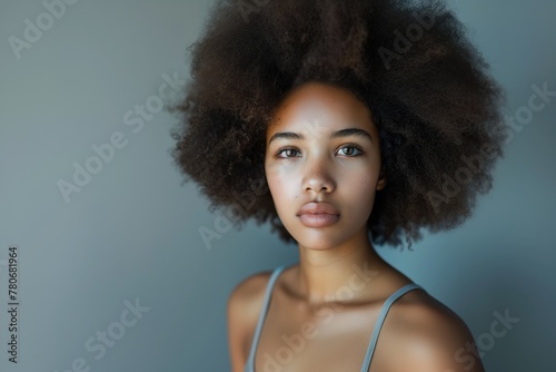 Young serious ethnic mixed latino or hispanic woman or girl with curly african american hair perfect skin, full lips and skincare looking at camera with neutral look in light studio