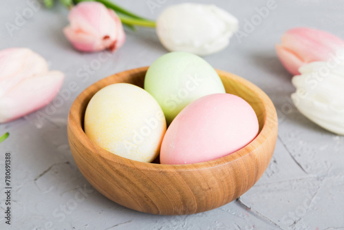 Happy Easter composition. Easter eggs in basket on colored table with yellow Tulips. Natural dyed colorful eggs background with copy space