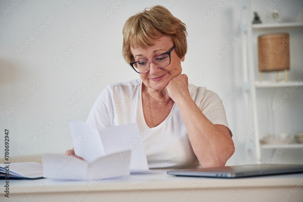 Reading the information from paper. Senior elderly woman is at home in the living room Reading the information from paper. Senior elderly woman is at home in the living room
