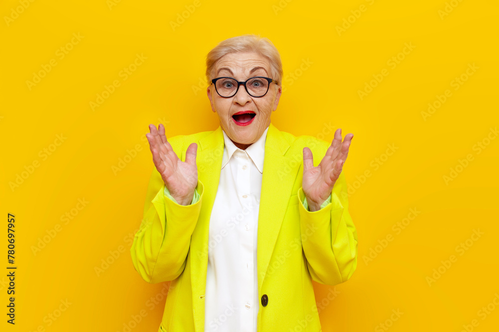 surprised old businesswoman in glasses and formal wear looks away in shock on yellow isolated background, elderly pensioner grandmother in blazer worries in amazement - obrazy, fototapety, plakaty 