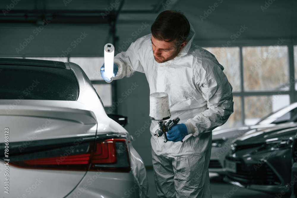 Rear part of automobile. Garage worker is holding lighting and checking surface of the car