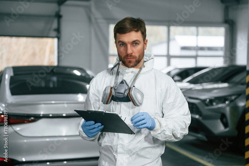 Portrait of car painter that is standing in the garage with documents in hands © standret
