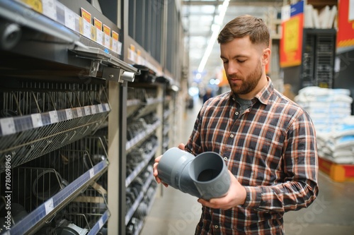 Handsome man choosing sewer pipes standing near the showcase of the plumbing shop photo