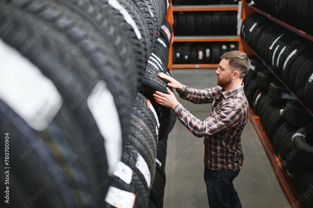 Fototapeta premium Male mechanic holding car tire in automobile store