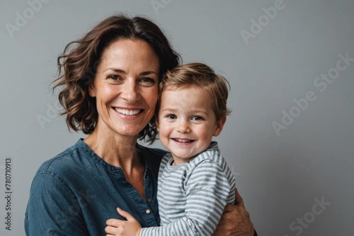 Smiling mother carrying young son while standing against gray wall at home