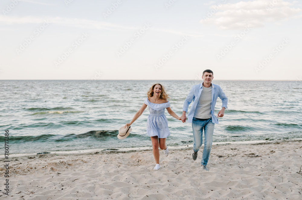Female and male run on beach ocean and enjoying summer day on vacation. Happy couple in love holding hands and looking at camera on seashore. Man and woman running on sand sea. Spending time together.