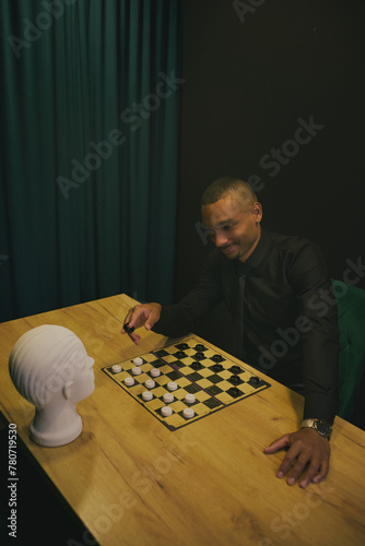 African American man playing checkers at table in team with head mannequin. Concept of business, strategies, competition