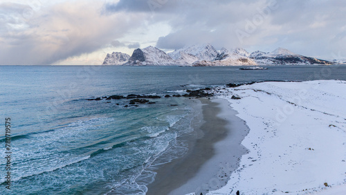 sanft treffen die Wellen auf den Strand bei Storsandnes, winter auf den Lofoten, Drohnenaufnahme von schneebedecktes Gebirge im Hintergrund photo