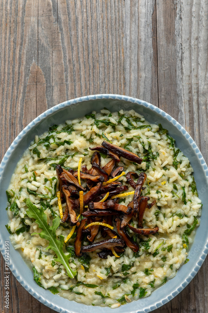 Lemon risotto with arugula and fried shiitake mushrooms in a blue bown on rustic wooden table. Copy space. Lemon risotto with arugula and fried shiitake mushrooms in a blue bown on rustic wooden table. Copy space.