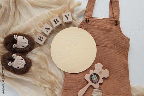 Round wooden disc mockup, pregnancy or baby waiting announcement template, baby name sign, flat lay composition with baby romper, shoes, rattle. photo