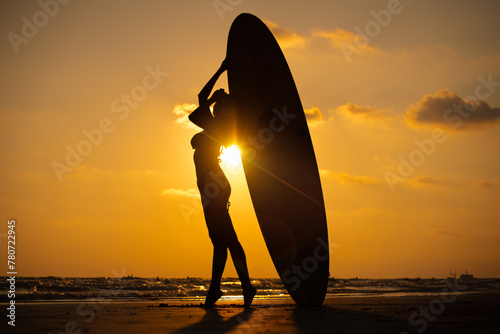 Silhouette sexy beautiful Asian model wearing bikini swimming suite posing happy on beach with surfboard is water sport game and hobby leisure in summer holiday lifestyle with sunset sky background.	