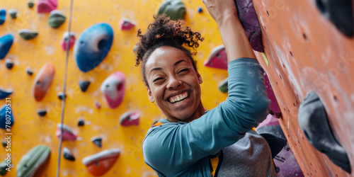 young athletic woman wearing sportswear climbing wall indoors, smiling portrait