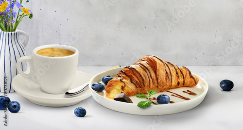 A croissant on a plate next to a cup of coffee