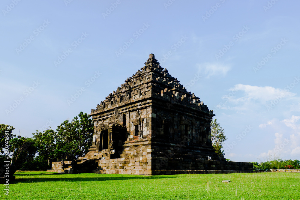 A large stone temple with a pyramidal roof, surrounded by lush green grass. The temple appears to be an ancient Hindu or Buddhist structure with architectural details. A large stone temple with a pyramidal roof, surrounded by lush green grass. The temple appears to be an ancient Hindu or Buddhist structure with architectural details.