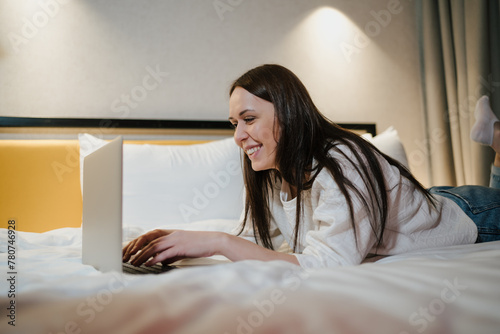 Smiling Young Woman Relaxing on Bed and Working on Her Laptop.
