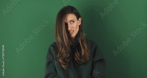 Crazy idea! Displeased girl in green sweater looking at camera with shocked frustrated expression and showing stupid gesture, accusing insane plan isolated on green background. Are you stupid? photo