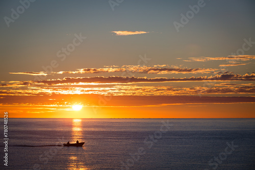 Silhouette of two people in a local small fishing boat moving with sunrise in the background on the Sea of Cortez near Los Barilles, Mexico on the Baja Peninsula.