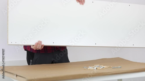 A carpenter man dressed in black pants and a red checkered shirt, assembling a white bookshelf. 4K UHD photo