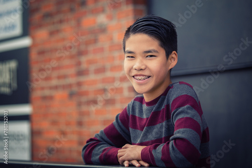 Happy, smiling teenage asian boy with braces leaning over outdoor railing.