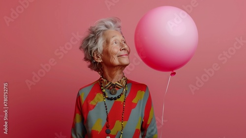 An elderly woman with a satisfied expression on her face looks at the balloon. the woman is dressed in arena attire with short gray hair. Horizontal studio photo with pink background.