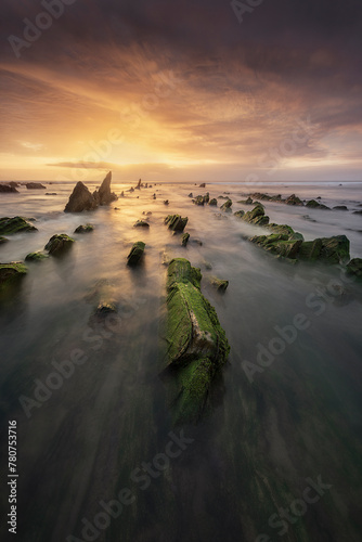 Fototapeta Naklejka Na Ścianę i Meble -  Flysch of Barrika beach, Bizkaia, at sunset with a dramatic sky of warm colors and the tide water entering between the rocks