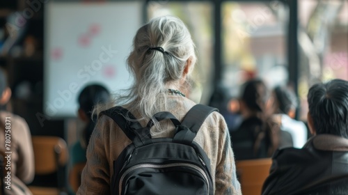 view from behind, a elderly woman with long hair carrying her black backpack in front of some people sitting on chairs watching the whiteboard at school  © cff999