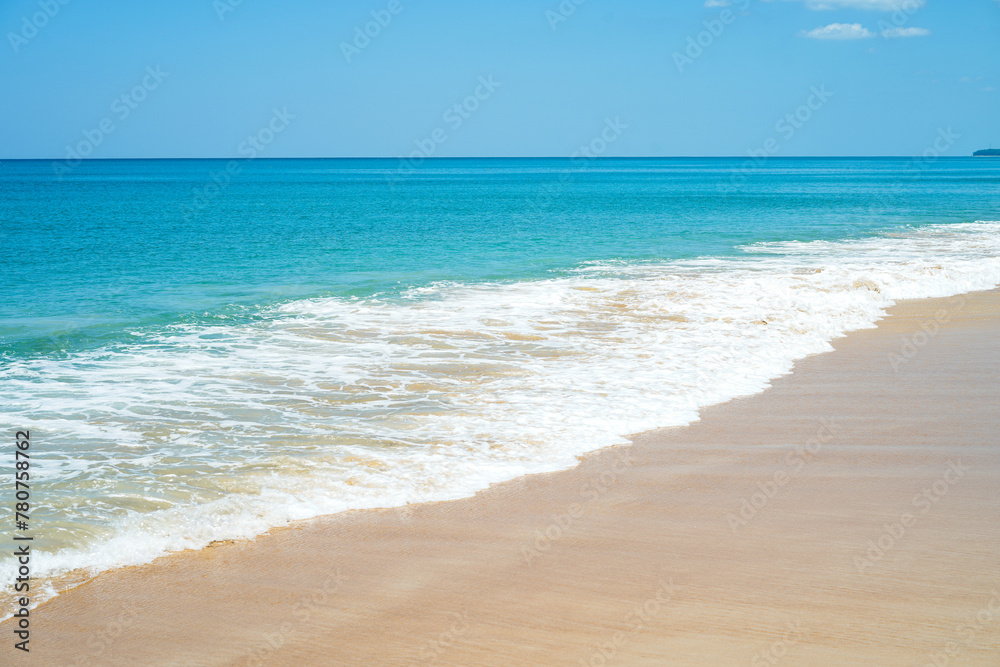 A scenic view of sandy beach and a long sea foam waves against blue sky with cloud with sunlight in the background in summer, presenting a breathtaking scenery in Mai Khao Beach, Phuket, Thailand.