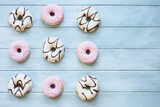 Flatlay of frosted vanilla donuts with chocolate swilrs and strawberry pink doughnuts with coconut flakes with copy space. Overhead table top view. Flatlay background.