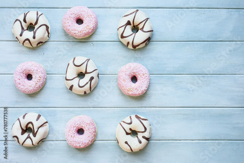Flatlay of frosted vanilla donuts with chocolate swilrs and strawberry pink doughnuts with coconut flakes with copy space. Overhead table top view. Flatlay background.
