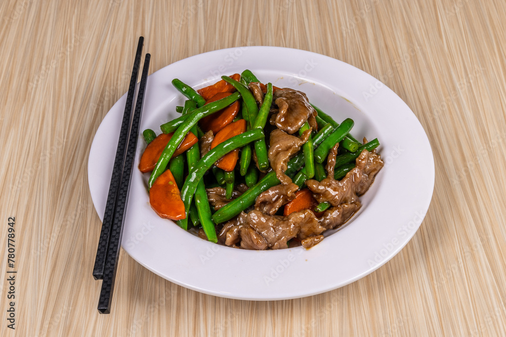 A plate of Chinese food, beef and green beans with vegetables with chopsticks on a wooden table