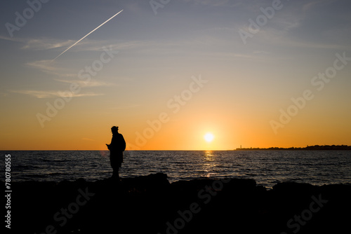Ragazzo gurda il tramonto dagli scogli a Marina di Ragusa