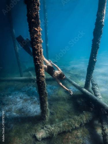 Woman freediver swims underwater in blue sea. Freediving between the pier pillars