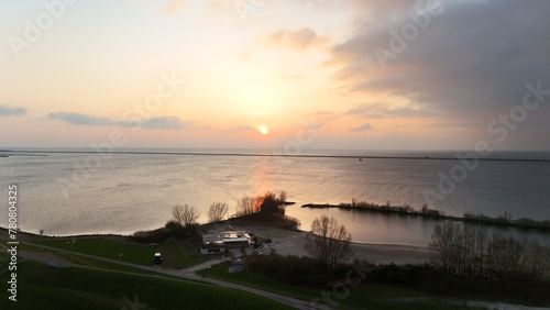 Scenic sunset over a tranquil lake with reflections on water, silhouette of a small peninsula with trees, and a clear sky, ideal for backgrounds and nature themes.