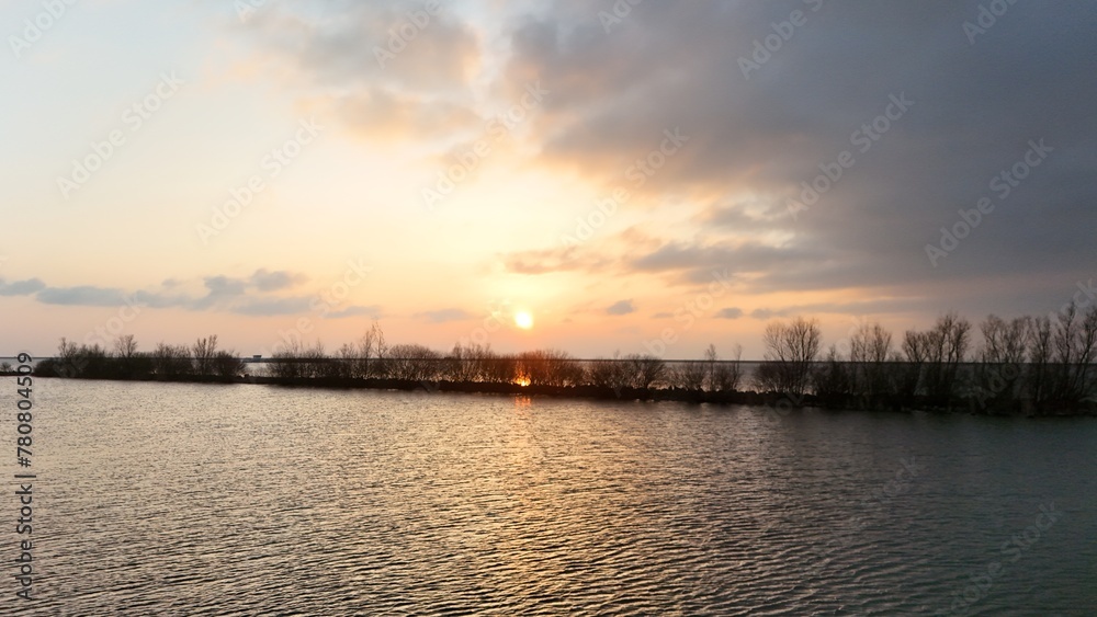 Serene sunset over a calm lake with silhouetted trees on the horizon under a soft gradient sky.