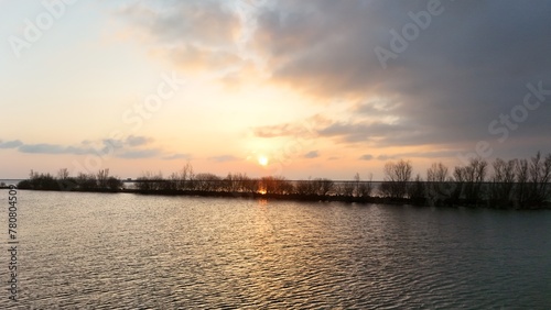 Serene sunset over a calm lake with silhouetted trees on the horizon under a soft gradient sky.