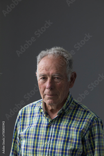 Vertical portrait of an older man with white hair and a plaid shirt with green tones.