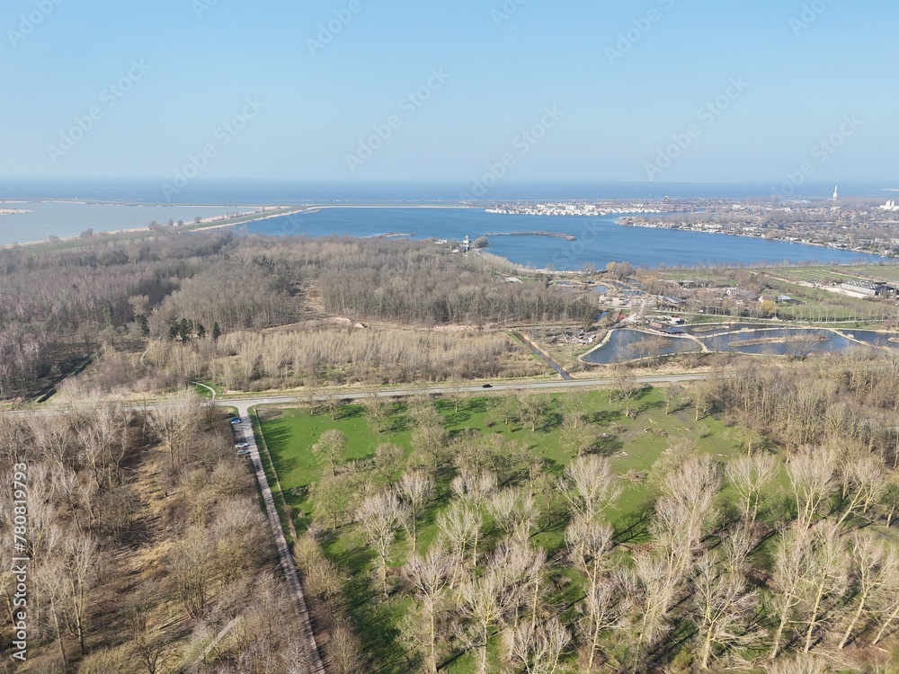 Aerial view of a coastal landscape with lush greenery, pathways, and a clear view of the blue sea merging with the sky on the horizon.