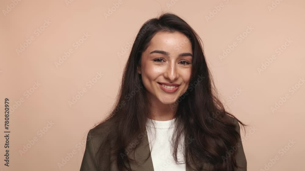 Portrait of a joyful woman with a playful wink and a warm, genuine smile against a soft beige backdrop, exuding positivity and charm. Portrait of a joyful woman with a playful wink and a warm, genuine smile against a soft beige backdrop, exuding positivity and charm.