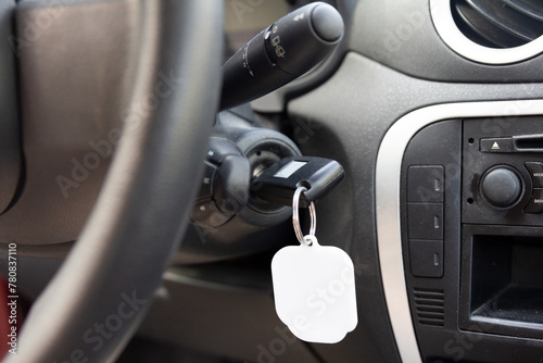 Close-up view of a car's ignition with a key inserted and a blank keychain, ready for branding or personalization, inside a vehicle interior