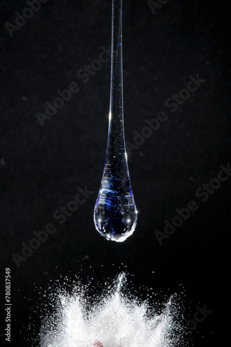 Gota de vidro azul semi transparente em fundo preto. Fotografia em close up de uma peça similar a um líquido de alta viscosidade pingando em cima de glitter branco.