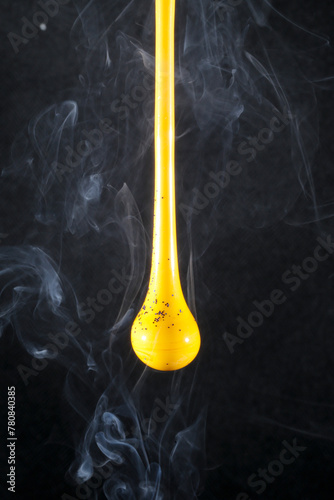 Gota de vidro amarelo semi transparente em fundo preto. Fotografia em close up de uma peça similar a um líquido de alta viscosidade pingando com fundo de efeito especial de cenário neutro.