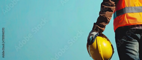 A construction worker stands sideways in a yellow protective vest and holds a helmet in his hands. Copy space. photo