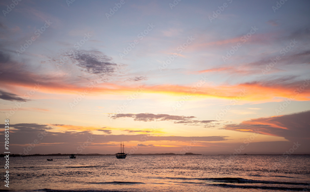 Pôr-do-sol na linha do mar, com barcos e navios no horizonte e degradê colorido de nuvens no nordeste brasileiro. Céu alaranjado e roxo. 