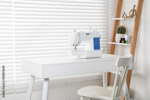 Sewing machine on white desk near chair indoors © New Africa