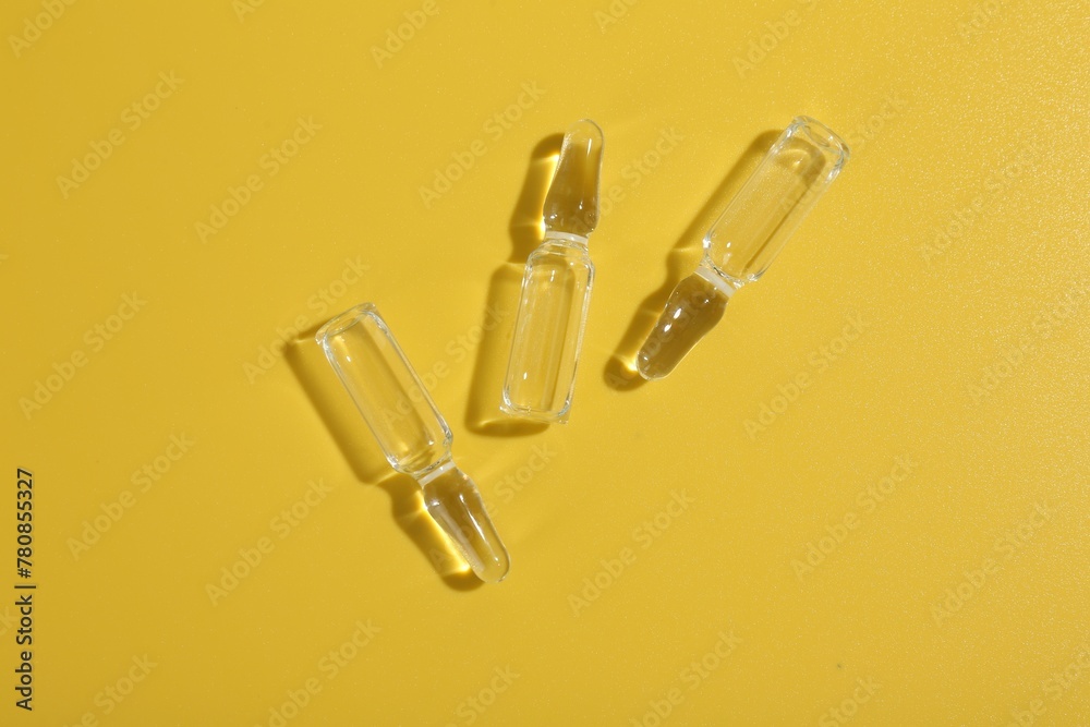 Naklejka premium Glass ampoules with liquid on yellow background, flat lay