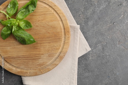 Wooden cutting board, fresh basil and napkin on grey table, top view. Space for text